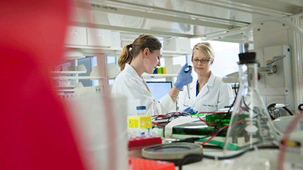 Genomic research students in white coats conducting experiments in a laboratory setting.