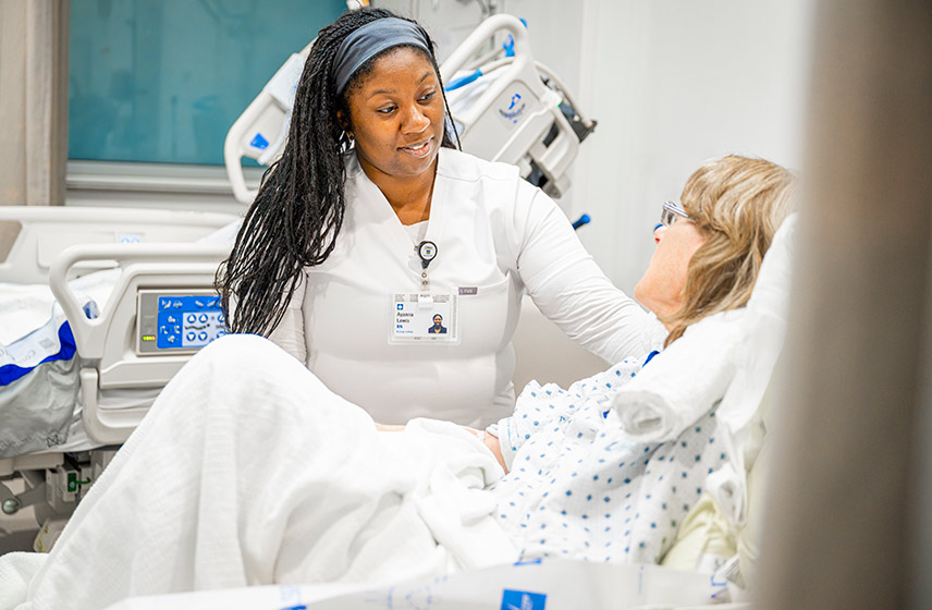 A Cleveland Clinic caregiver speaking with a patient in a hospital bed.