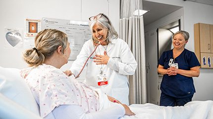 Nurse and nurse shadow checking on a patient in a hospital room.
