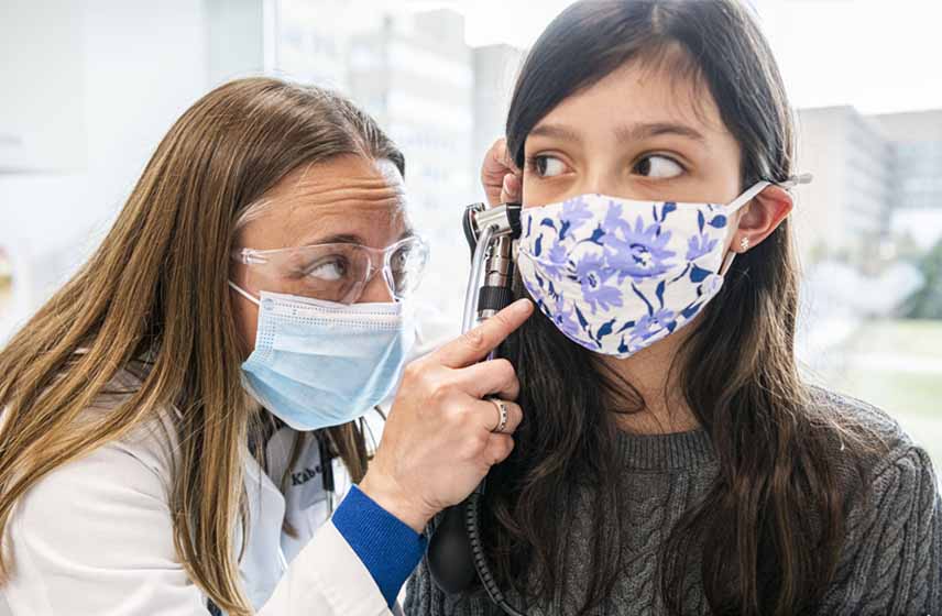 Pediatrician examining young girl's ear drum and outer ear canal with otoscope.